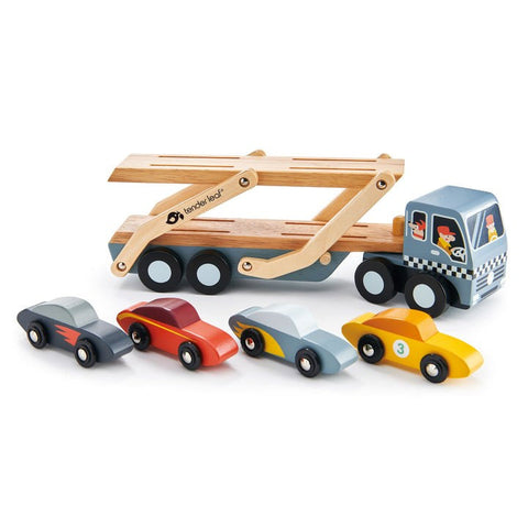 The Tender Leaf Car Transporter by Tender Leaf is a wooden toy featuring a multi-colored car transporter. It includes a truck with a detachable trailer and four vibrant super cars in blue, yellow, red, and gray. The trailer is equipped with two wooden loading ramps, and the truck's cabin is detailed with illustrations of drivers.