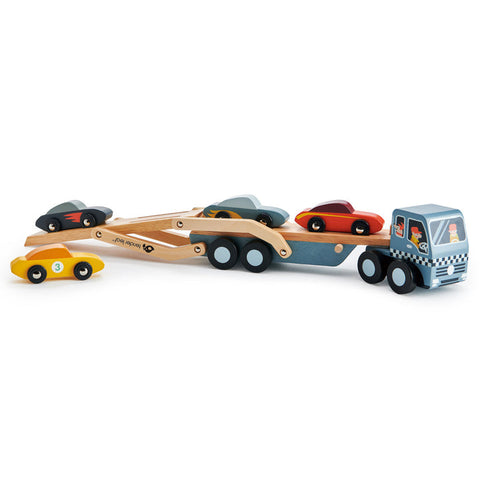 The Tender Leaf Car Transporter by Tender Leaf is a wooden toy car carrier truck featuring an extendable, two-tier trailer that holds four colorful super cars (black, yellow, red, and dark blue). The truck cabin is adorned in gray and blue with playful face designs and traffic light motifs. Each car is crafted to fit perfectly on the wooden transporter.